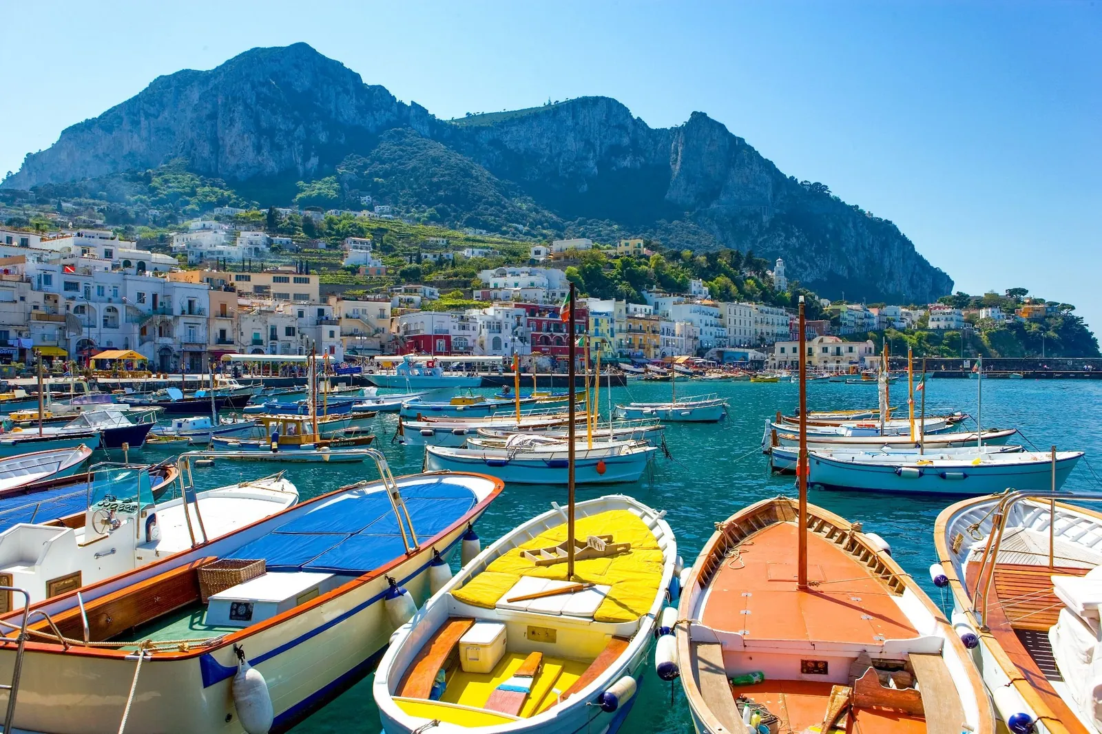 White boats in the brilliant blue water beneath the Faraglioni rocks of Capri